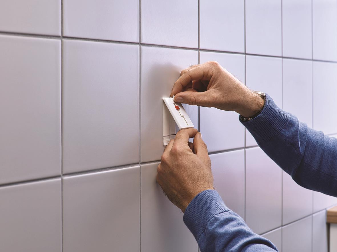 Person applicerar självhäftande Tesa Powerstrips på kakelvägg