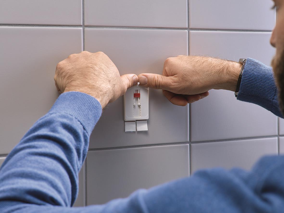 Person fäster självhäftande spik Tesa Powerstrips på kakelvägg