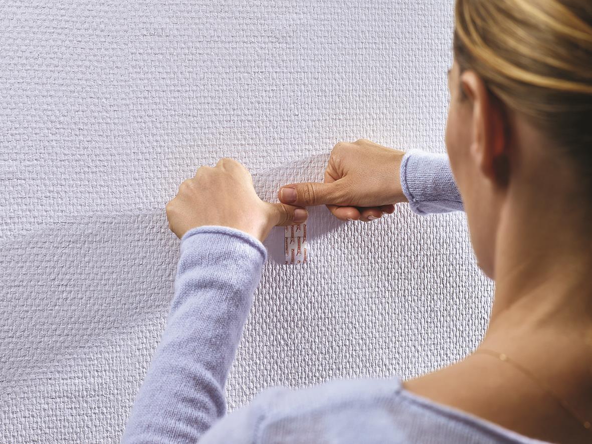 Person som sätter upp självhäftande Tesa Powerstrips på tapet eller gipsvägg