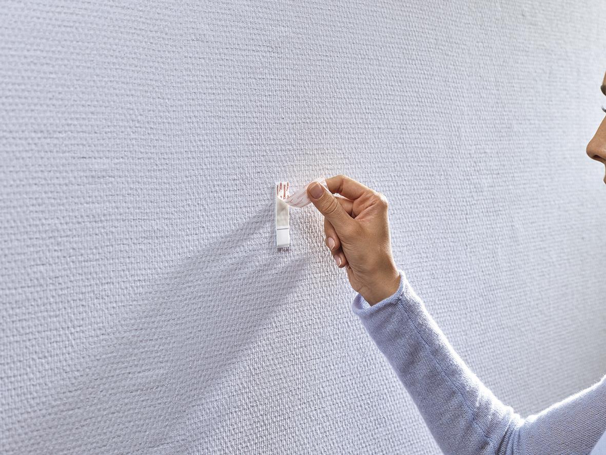 Person fäster Tesa Powerstrips på tapet eller gipsvägg