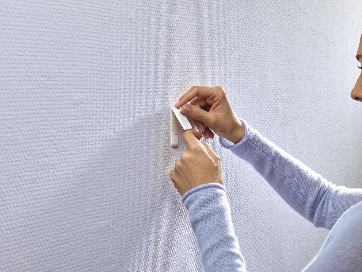 Person fäster Tesa Powerstrips på tapet eller gipsvägg