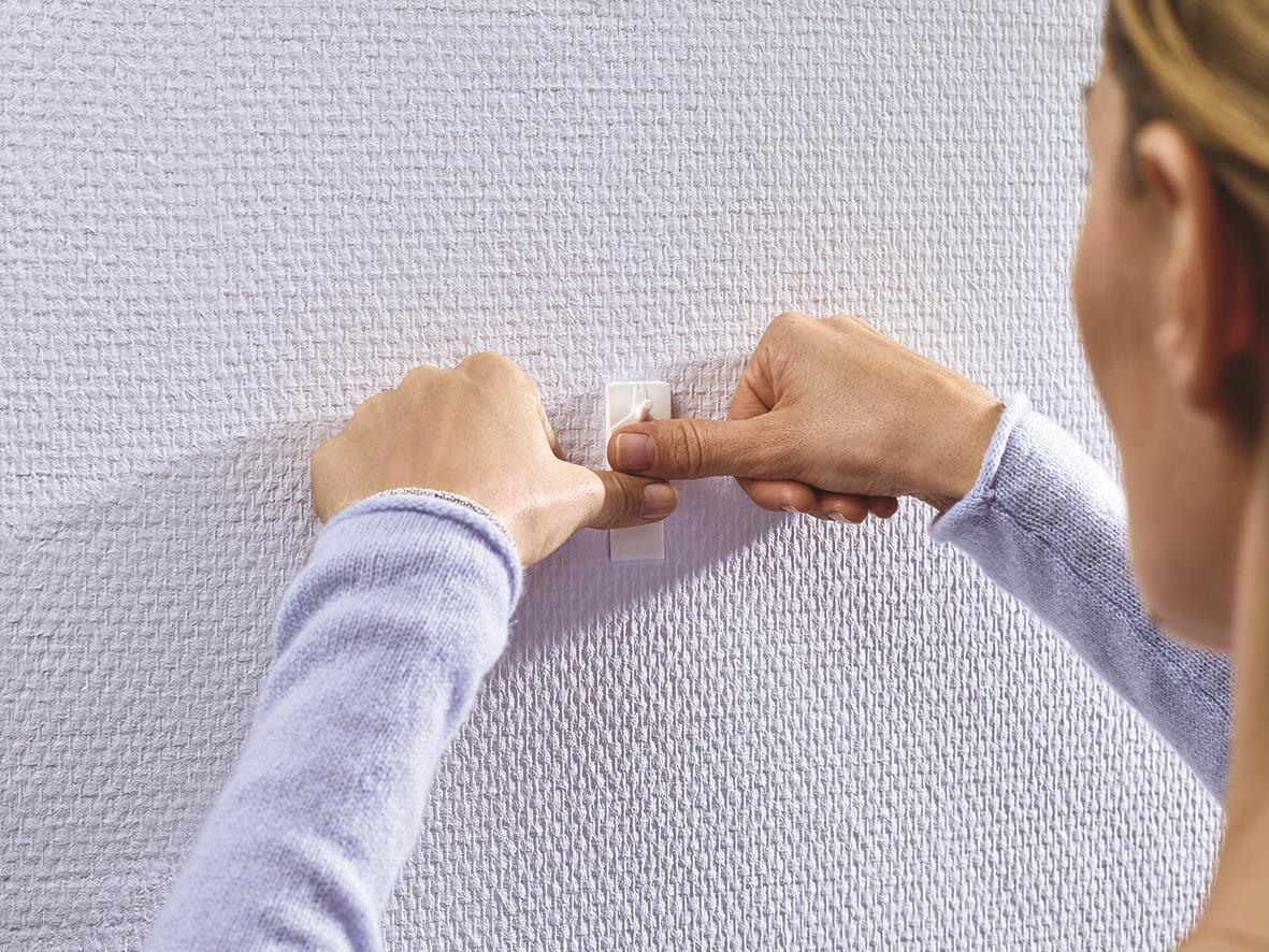 Person som fäster Tesa Powerstrips på en vägg