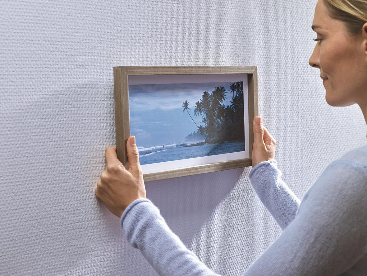 Kvinna hänger en bildram på tapet med självhäftande Tesa Powerstrips