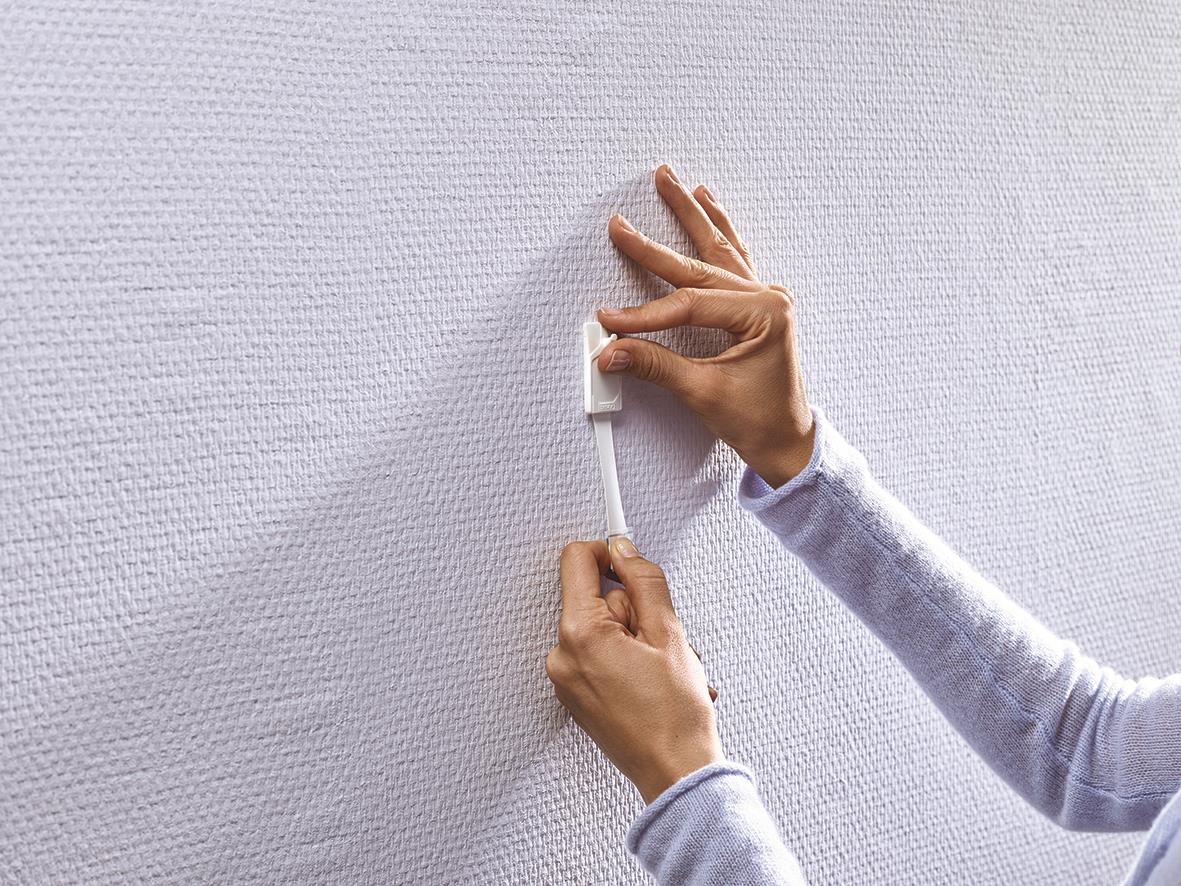 Person använder Tesa Powerstrips för att fästa något på tapet eller gipsvägg