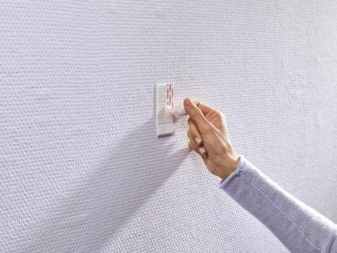 Hand som sätter upp en självhäftande Tesa Powerstrips på en vägg