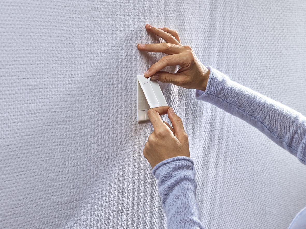 Person som fäster en självhäftande Tesa Powerstrip på en vägg