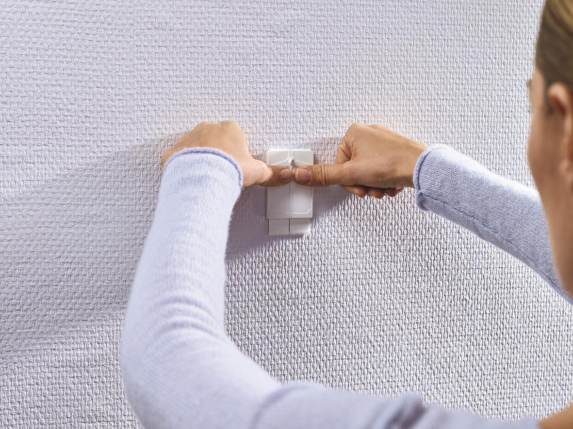 Person fäster Tesa Powerstrips på tapet eller gipsvägg