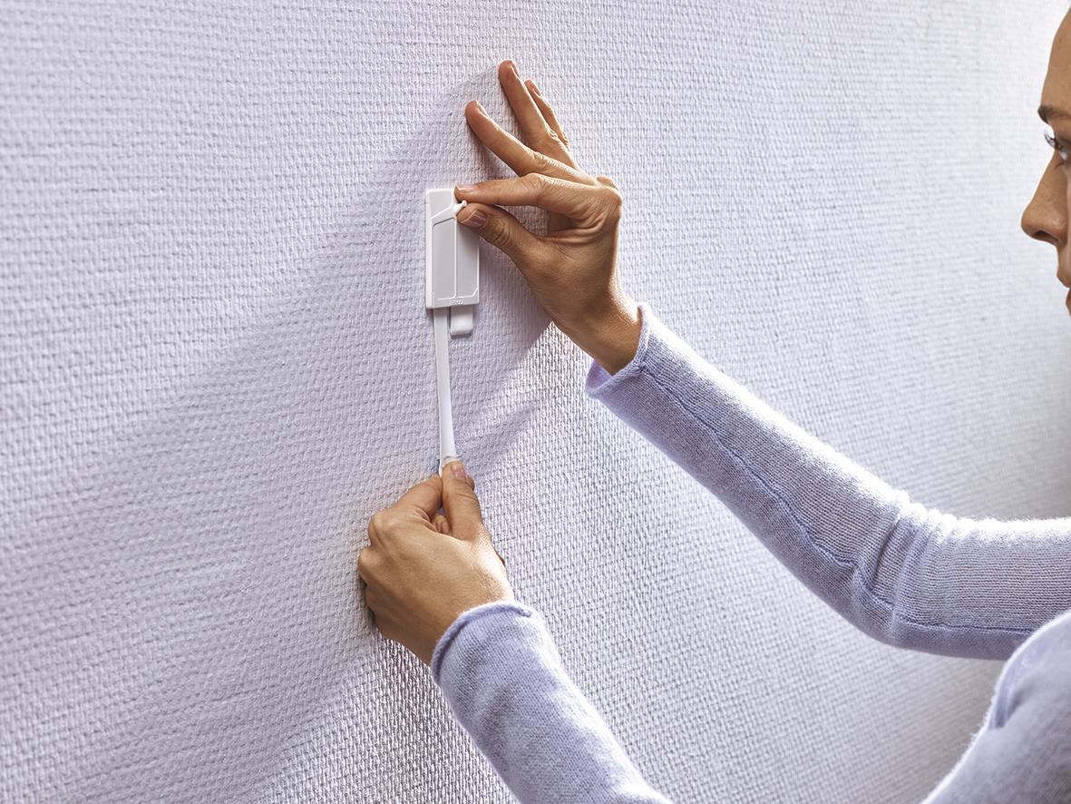 Person som fäster Tesa Powerstrips på en vägg