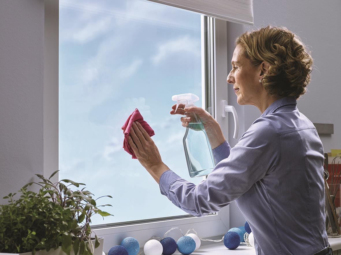 Kvinna rengör fönster med spray och trasa inomhus