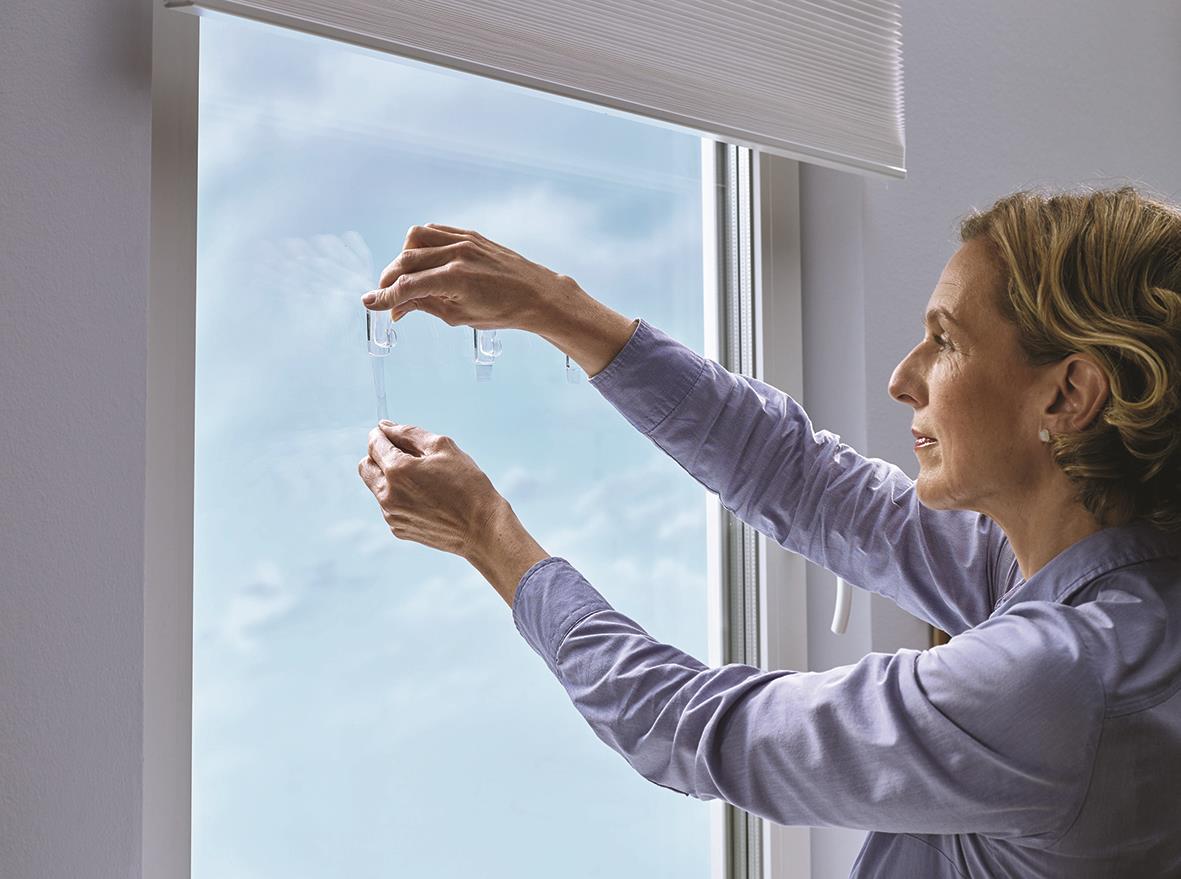 Kvinna fäster en självhäftande krok på fönstret med Tesa Powerstrips