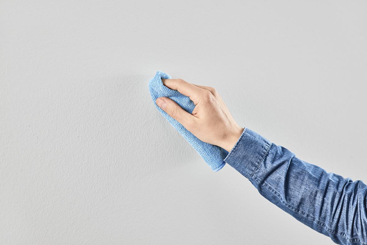 Hand som torkar en vit tapet eller gipsvägg med en blå trasa