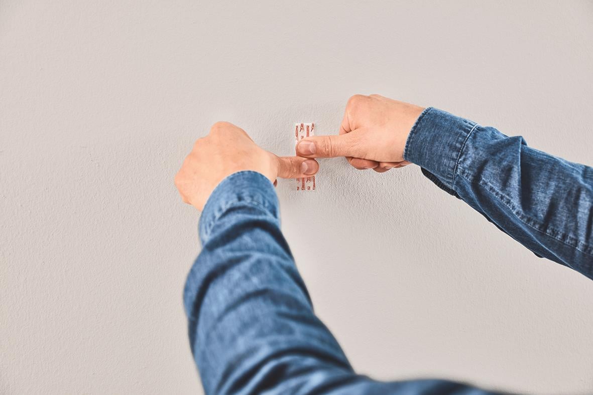 Person fäster en självhäftande krok på en vägg