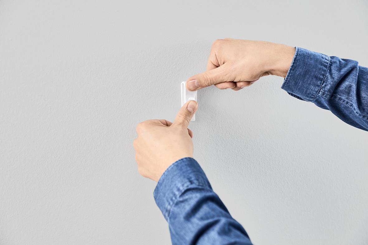 Person som applicerar en självhäftande krok på en vägg