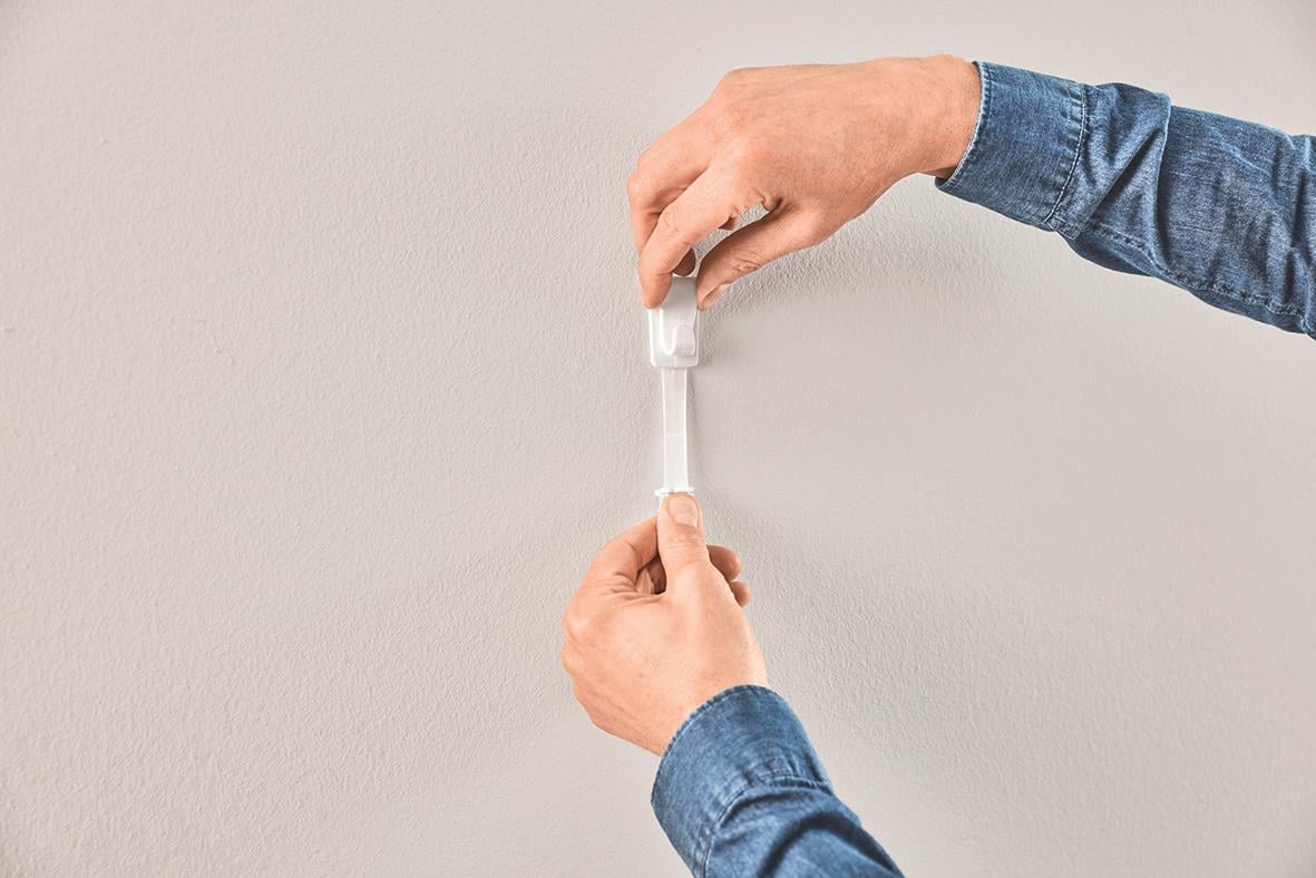 Person som applicerar en självhäftande krok på en vägg med tapet eller gips