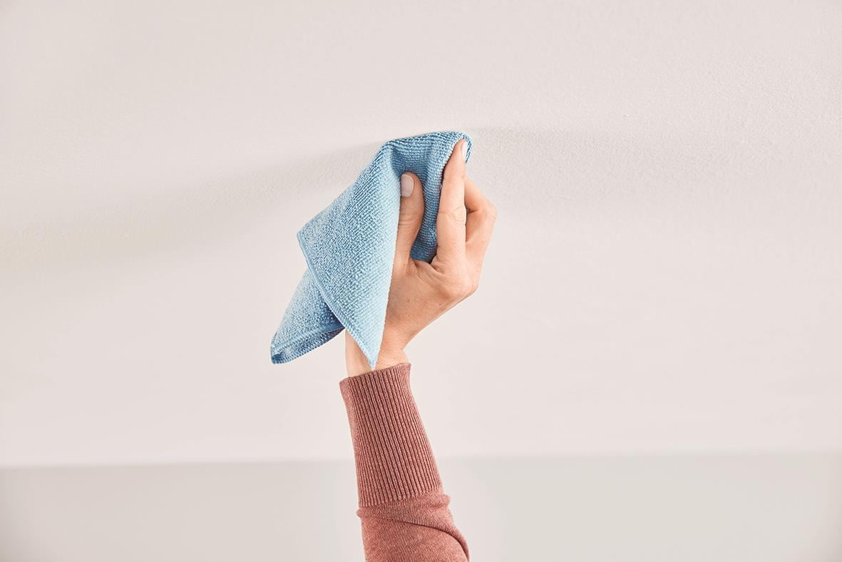 Hand som rengör en vit vägg med en trasa, används för att fästa saker med självhäftande takkrok