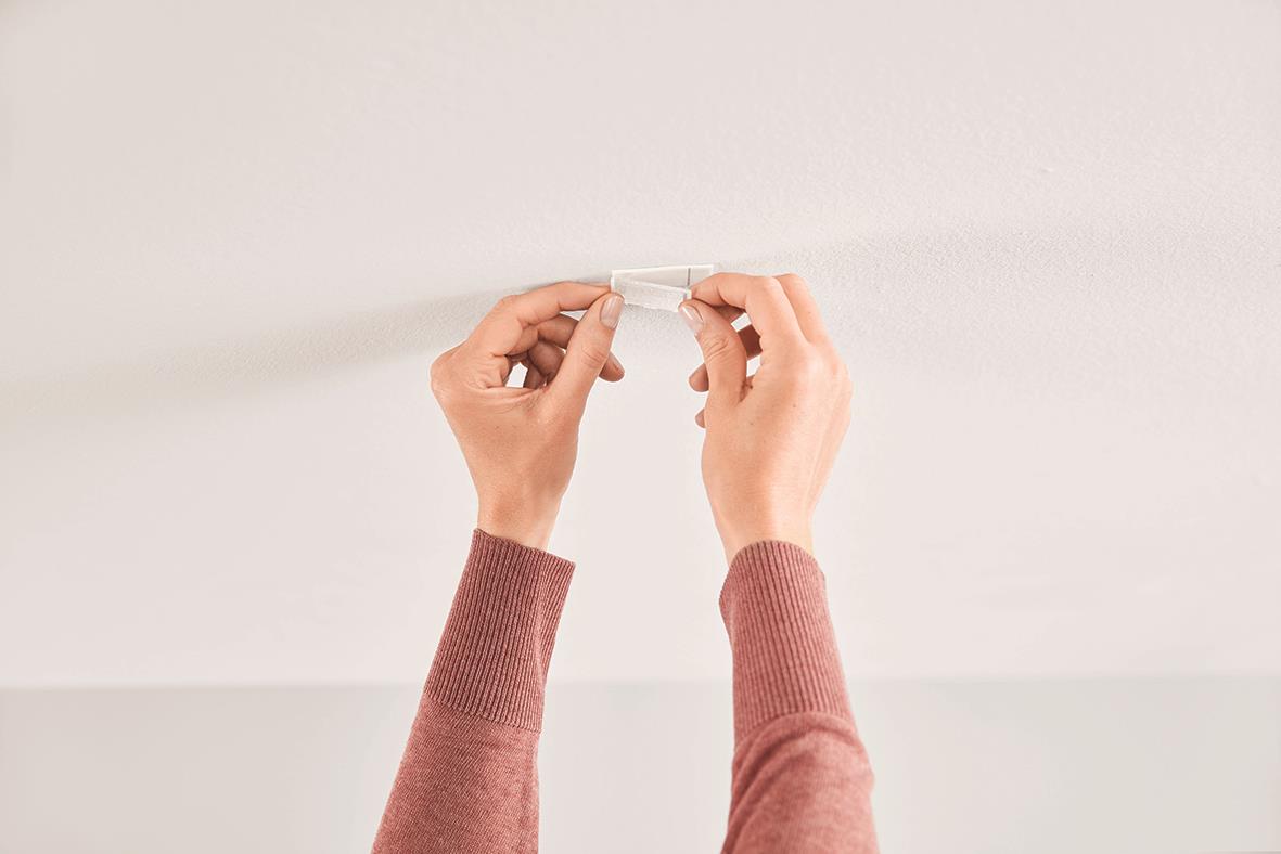 Person monterar en självhäftande takkrok på en vit vägg