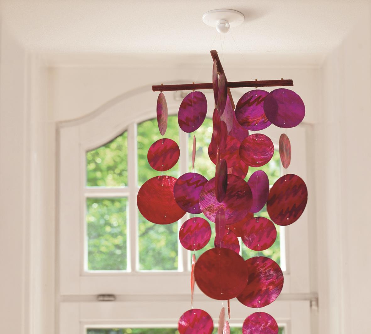 Färgglad mobil av papper eller plast hängande i ett rum framför ett fönster med grönt utomhus