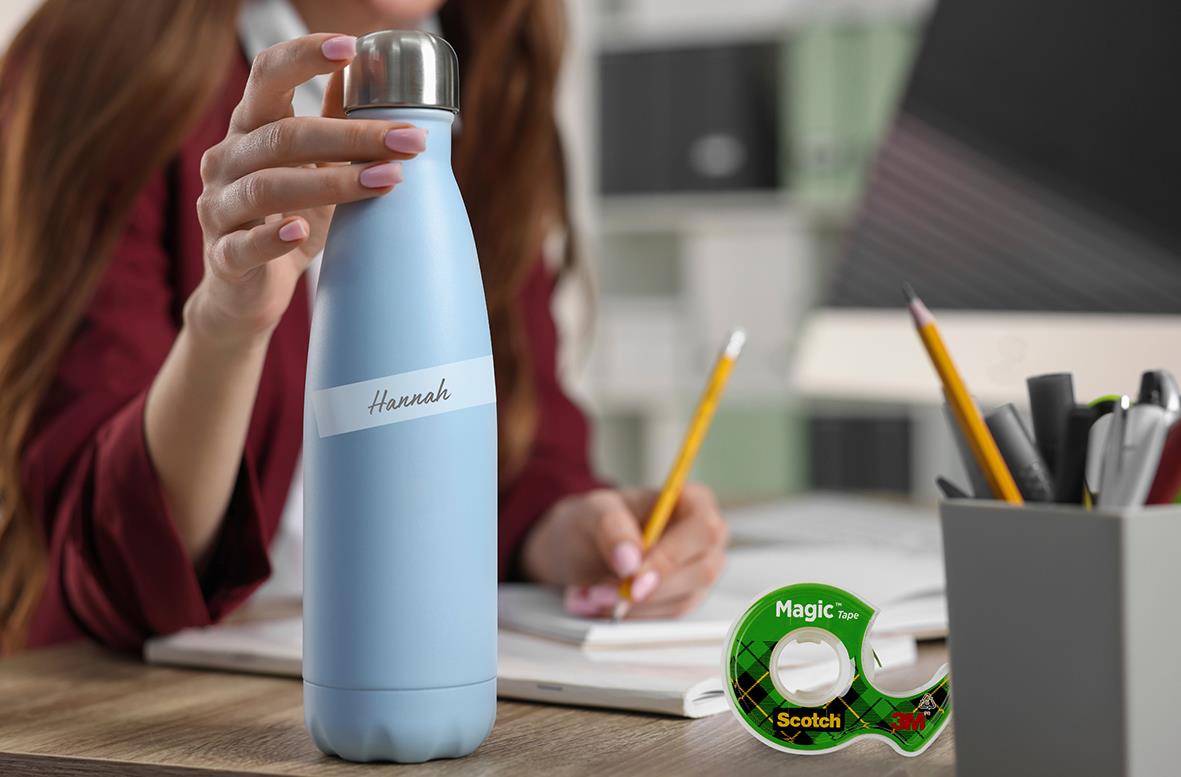 Person som skriver med penna vid skrivbord med vattenflaska och Scotch Magic tejp