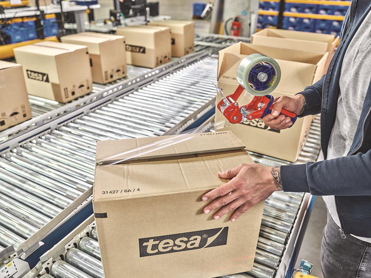 Person som packar en kartong med Tesa Eco & Ultra Strong packtejp på ett produktionsband