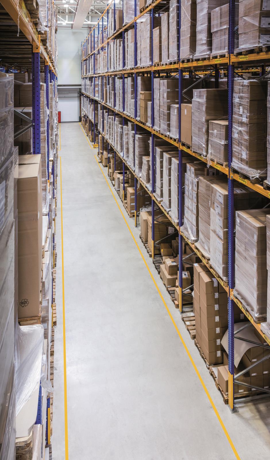 Lagerhylla med många kartonger och förvaringslådor i ett lager med tydliga gula markeringar på golvet