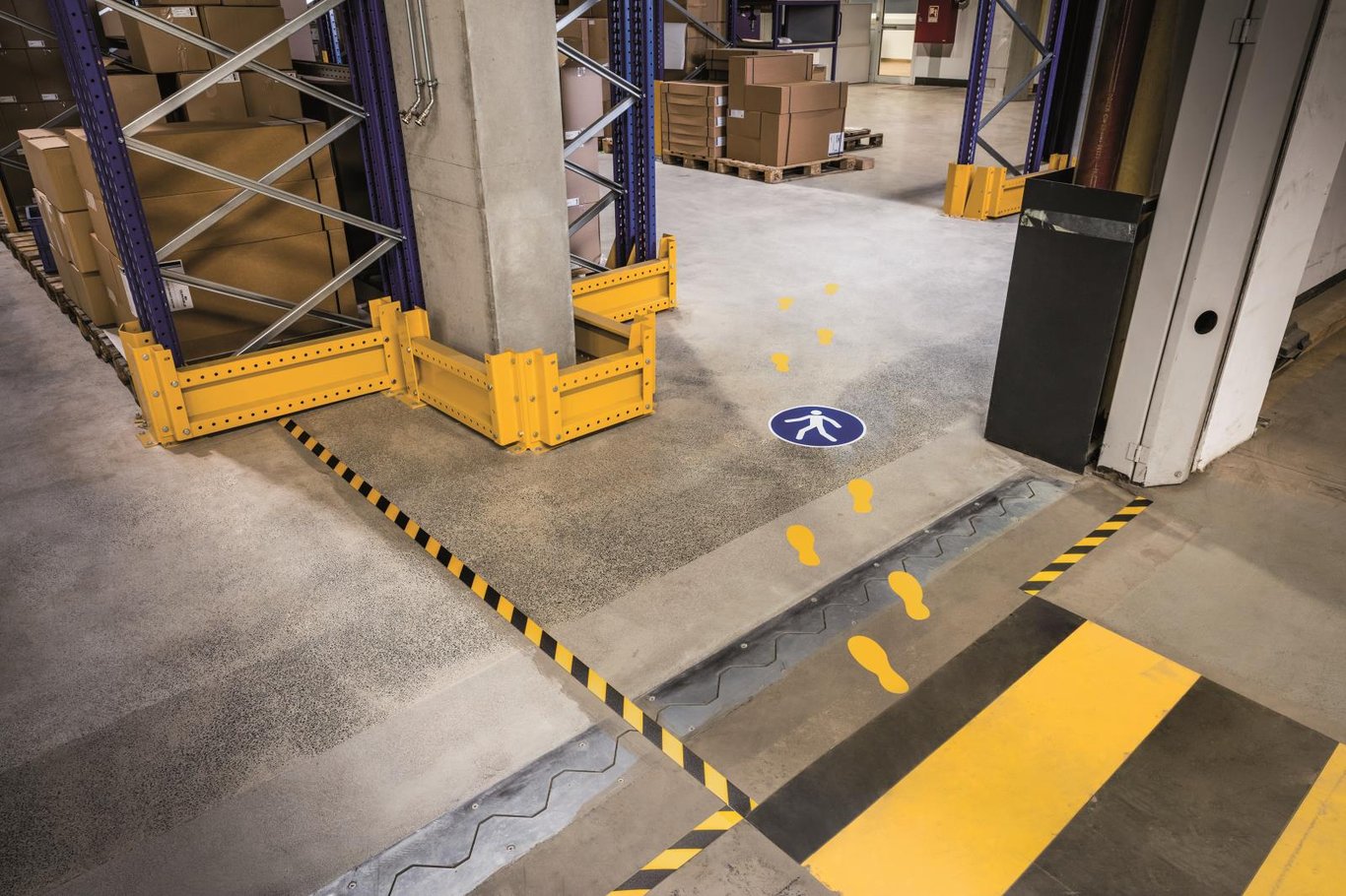 Varningstejp på golvet i lagerlokal, gul och svart, markerar farligt område och gångväg