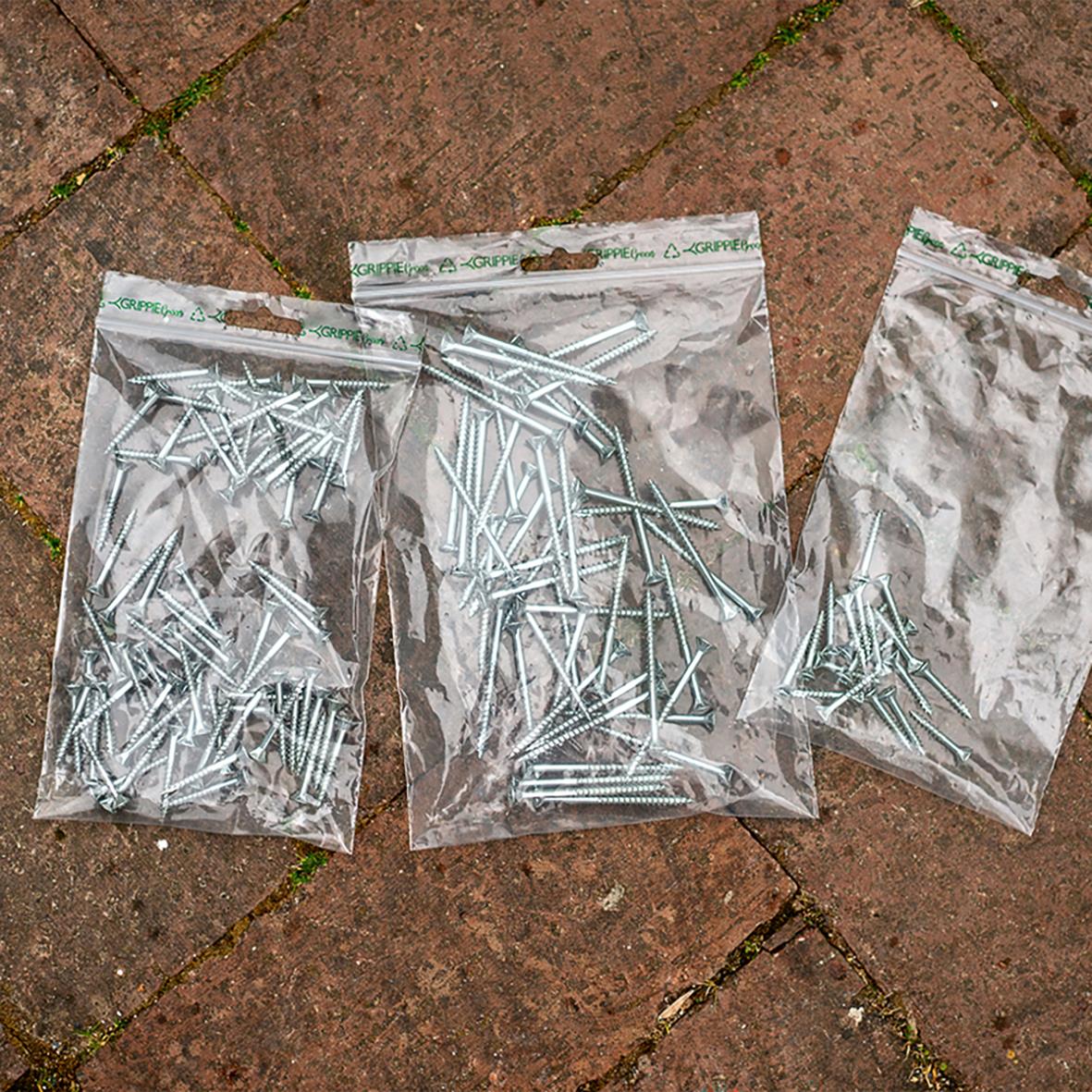 Tre plastpåsar med gröna blixtlåspåsar utan skrivfält, olika storlekar, på en tegelplattor