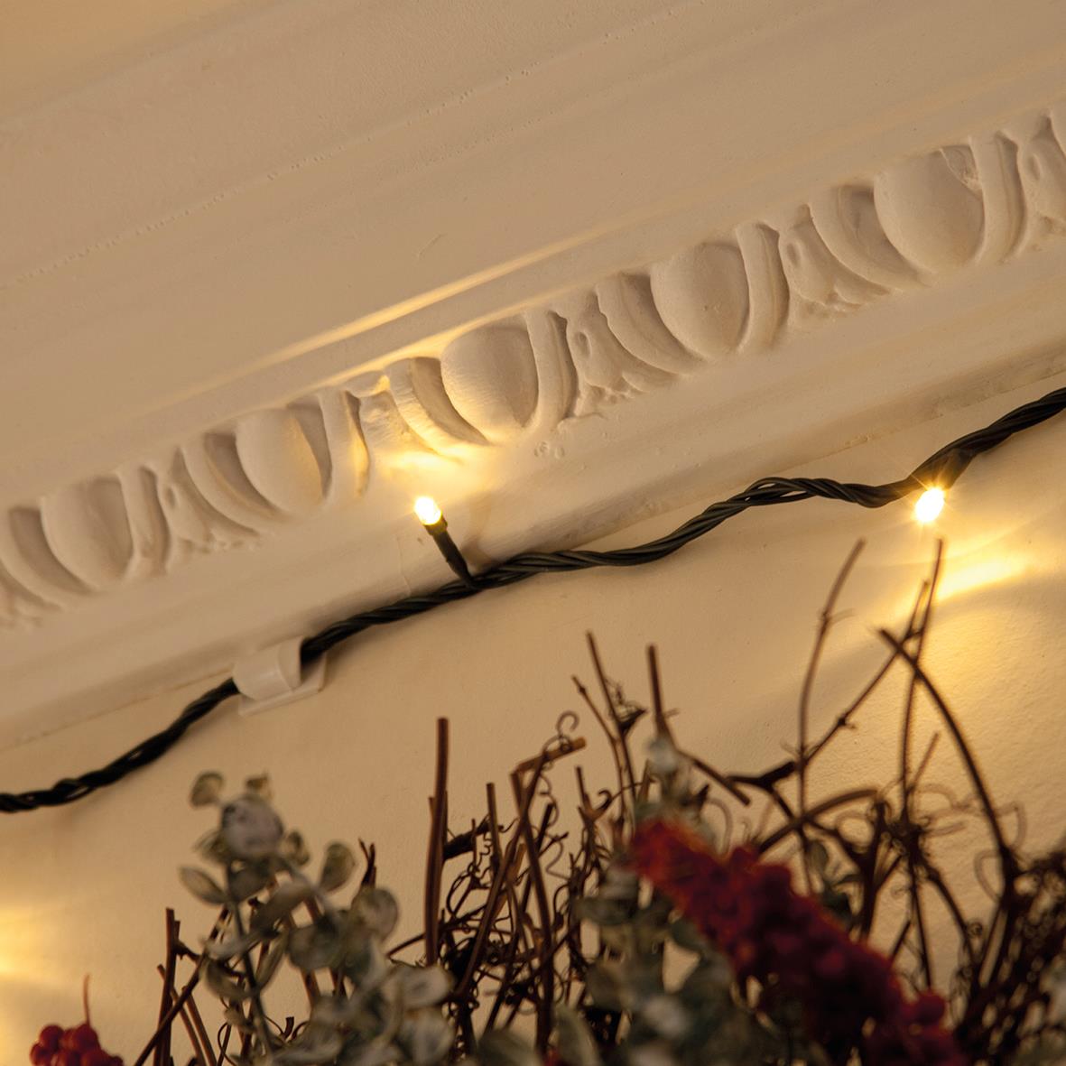 Vit kabelklämma D-LINE på vägg under tak med dekorativa element och ljusslinga