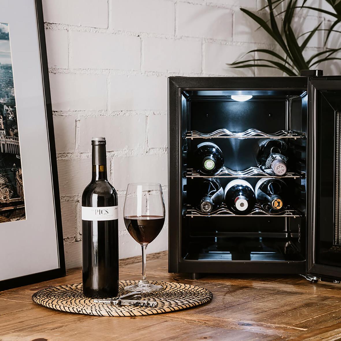 Vinkyl Taurus Chanson 12 flaskor med vinflaska och glas på träbord framför vit vägg