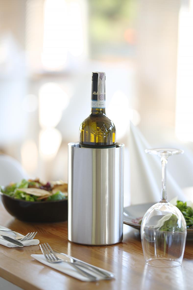 Vitt vin i en kyl på ett bord med sallad, bestick och ett tomt glas, i ett ljusrum.