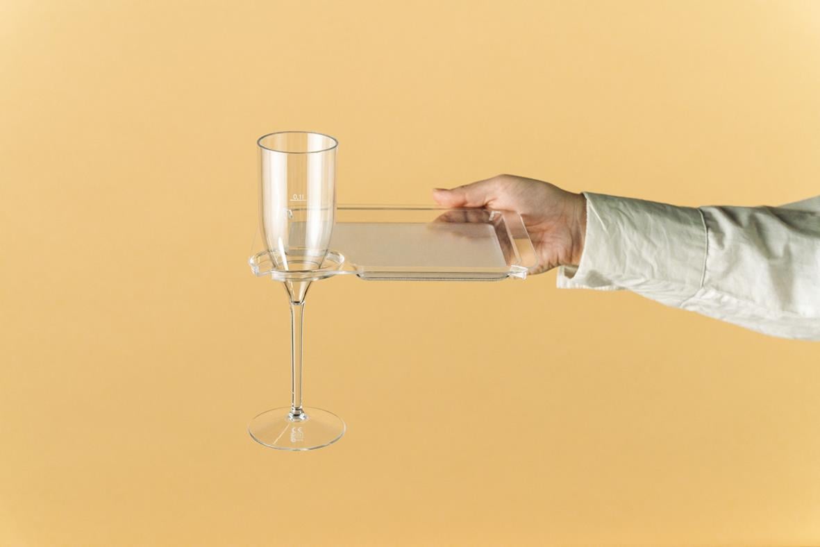 Person håller en transparent tallrik med glasfäste för glas på en beige bakgrund