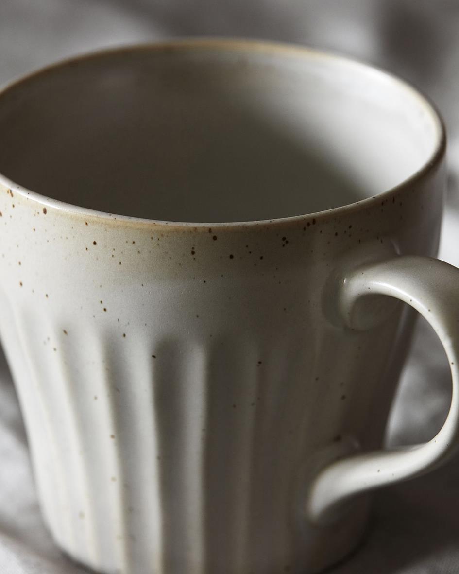Beige mugg med avlånga ränder och liten fläck på kanten, fylld med dryck
