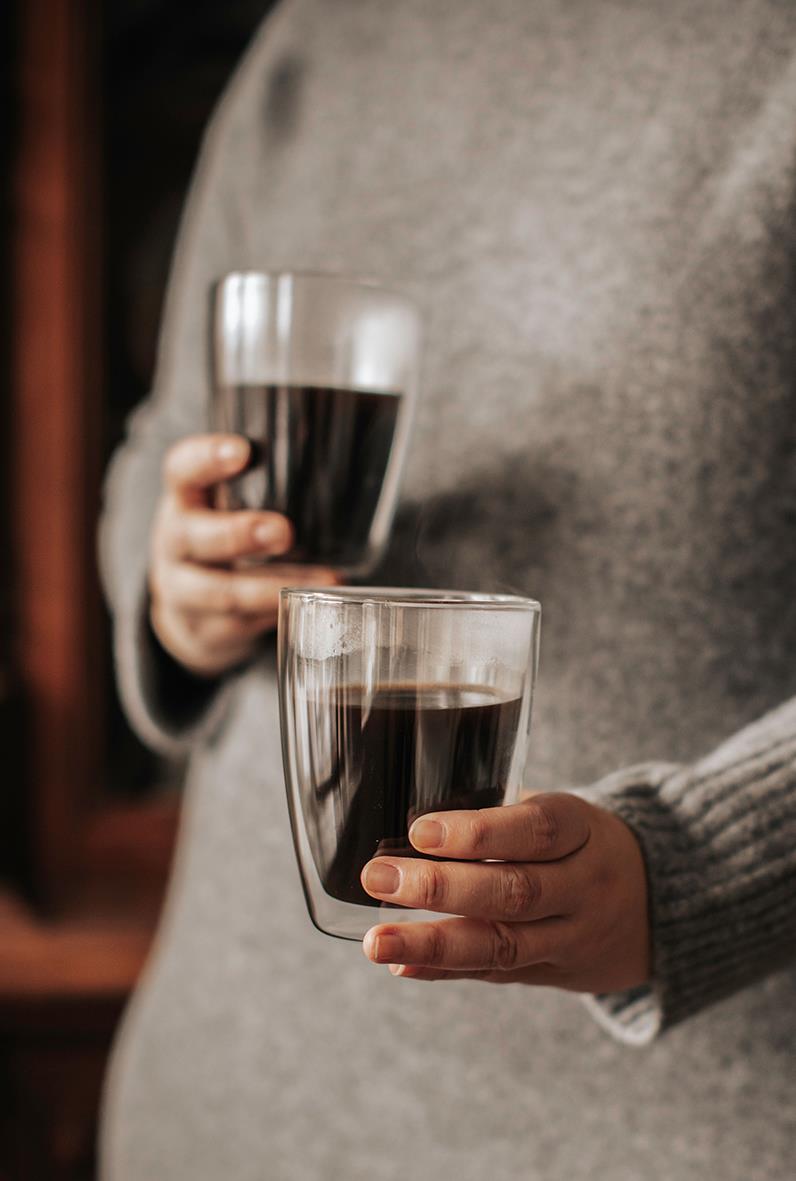 Person som håller i två kaffemuggar med svart kaffe, en i varje hand, i ett inomhusmiljö