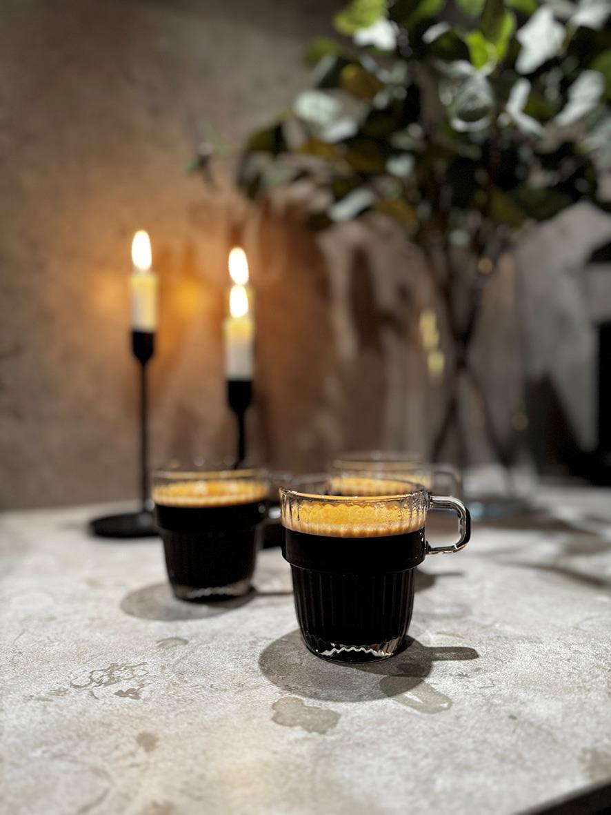 Två kaffemuggar av Bormioli Rocco Barshine på ett bord med ljus och växt i bakgrunden