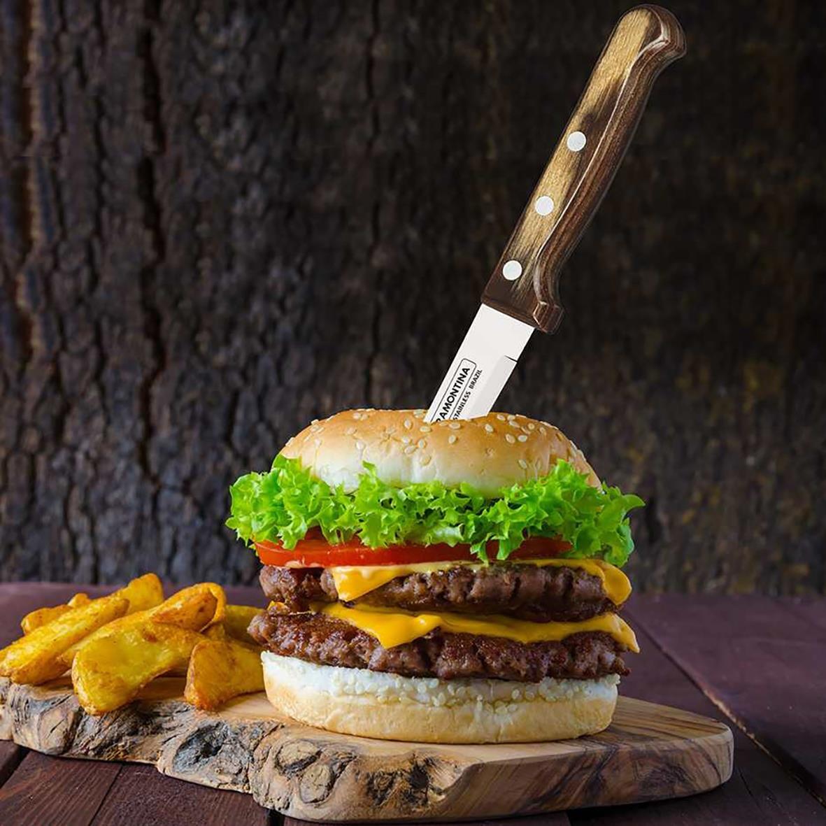 Grillkniv stuck i en hamburgare med sallad, tomat och köttfärsbiff, på en träskiva