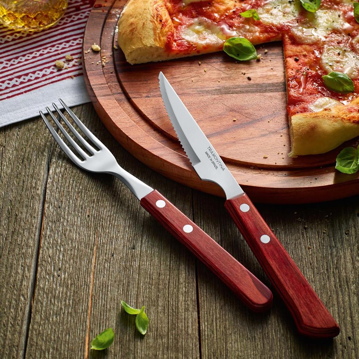 Grillgaffel och kniv med röda handtag på träbord bredvid pizza