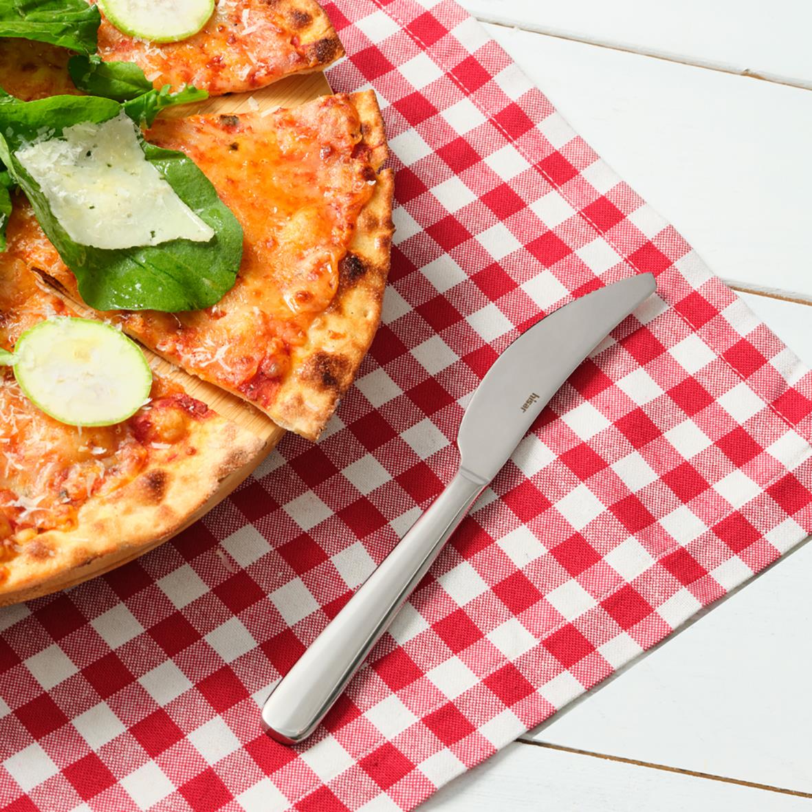 Pizza på ett rött och vitt rutigt underlägg med en matkniv bredvid