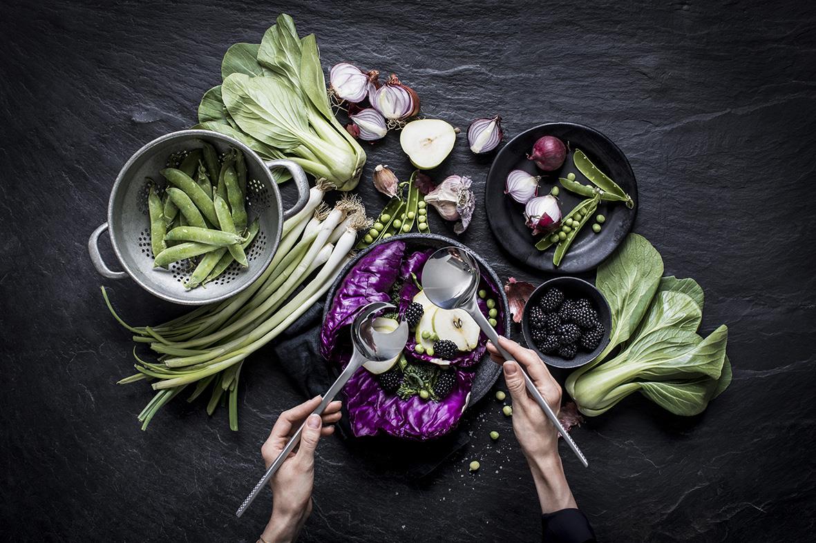 Person som använder salladsbestick för att servera grönsaker och bär på en mörk bakgrund