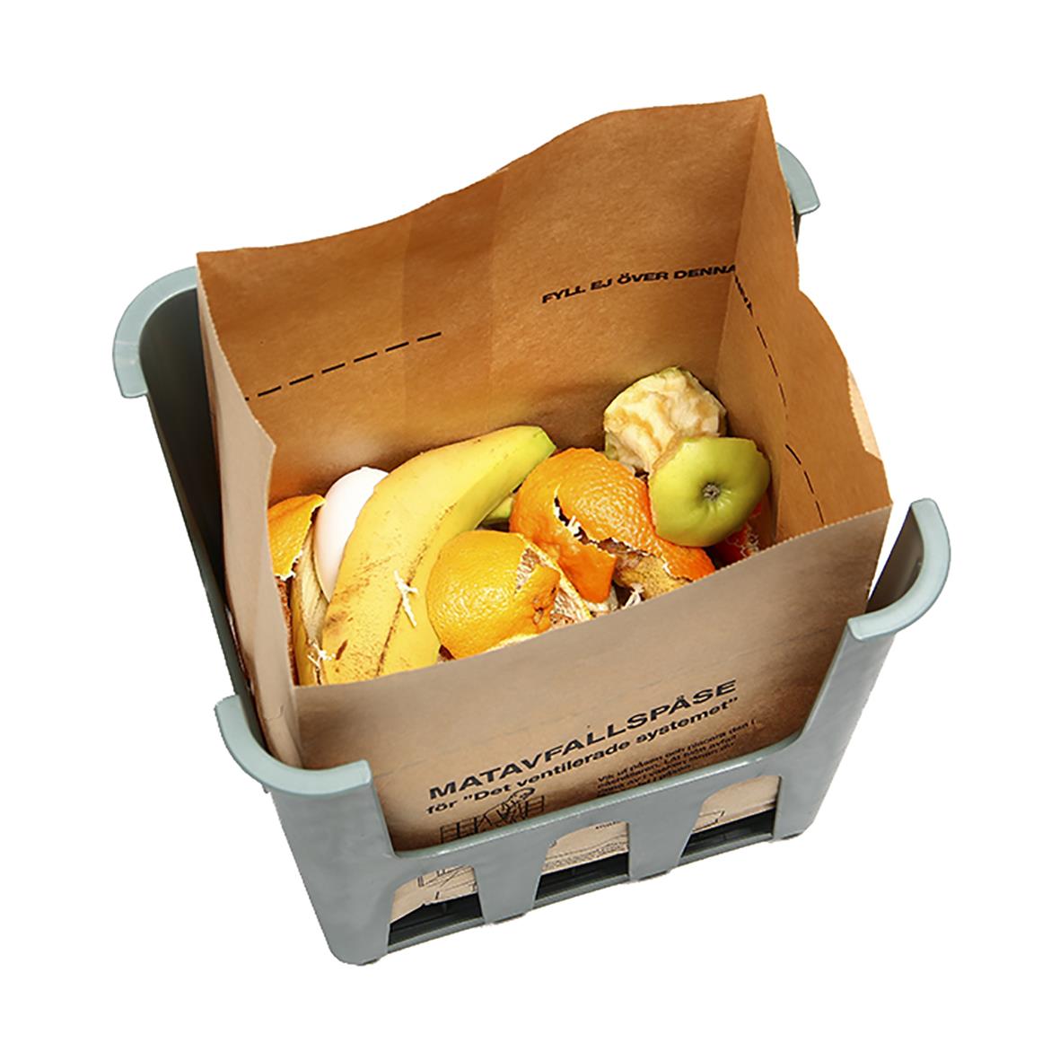 Matavfallskorg med frukt och matrester i en grå plastkorg med papper för matavfall