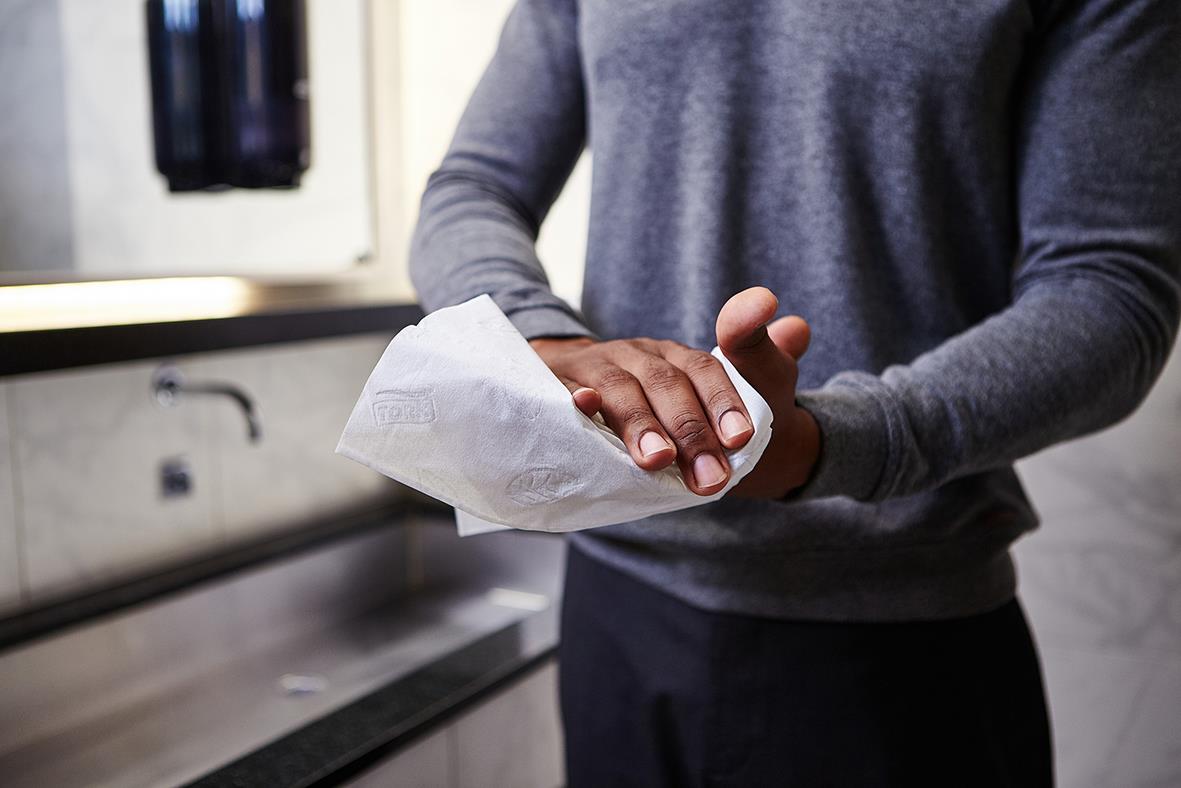 Person torkar händer med pappershandduk i kök eller arbetsmiljö