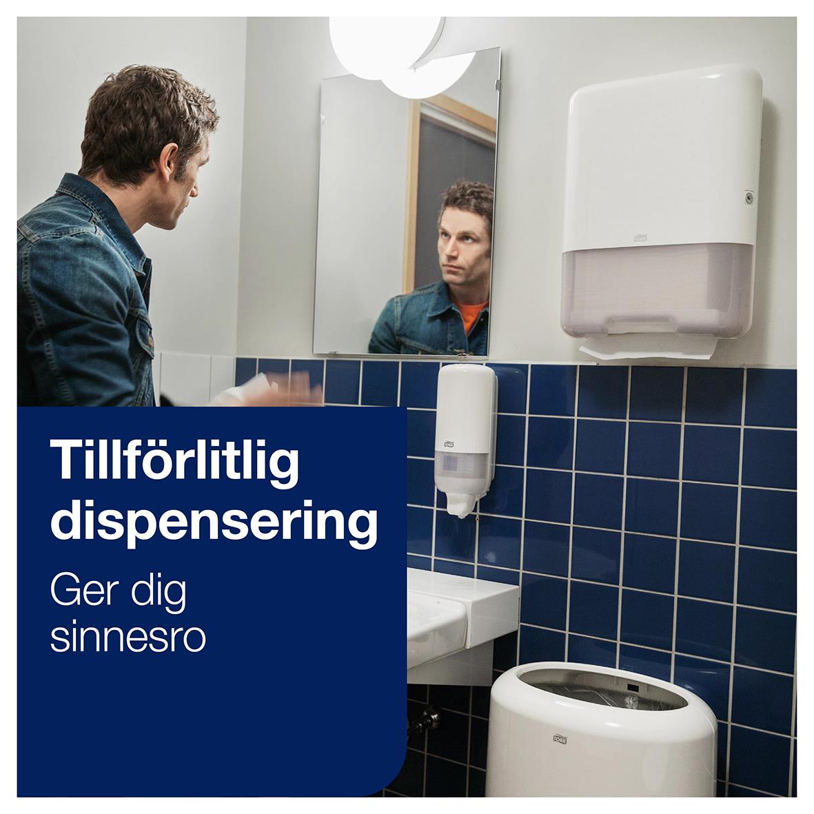 Man tittar i spegel i badrum med pappershanddukshållare och tvättställ