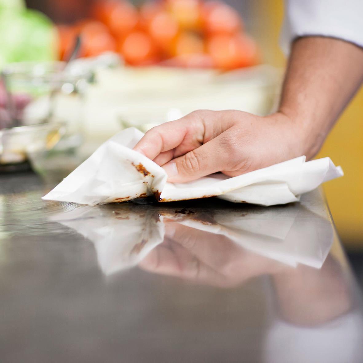 Hand som torkar av en köksbänk med vitt hushållspapper