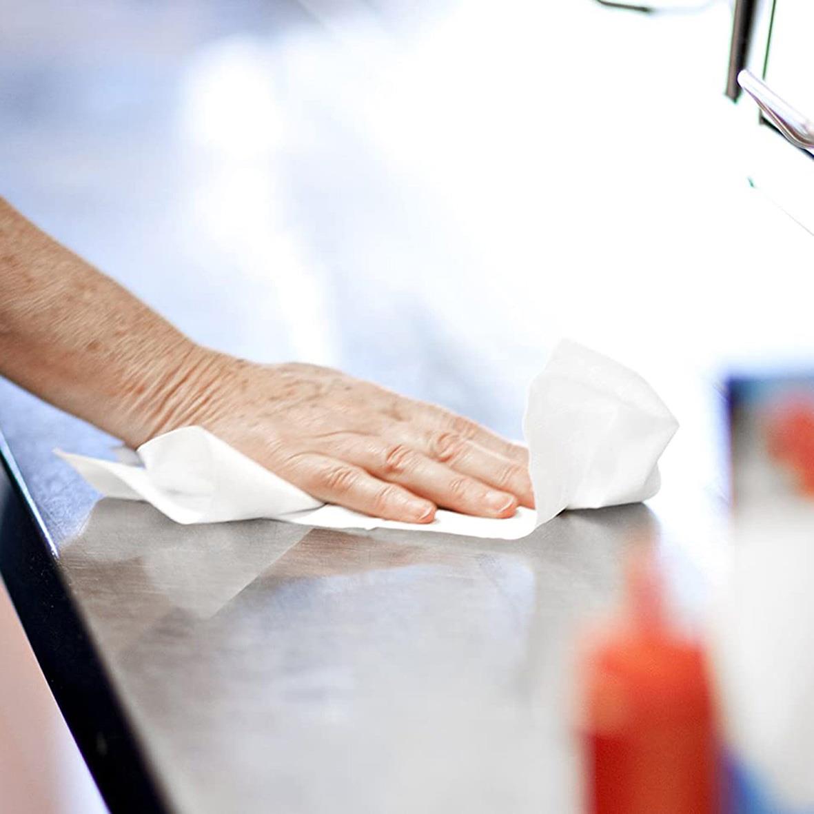 Hand som torkar en yta med hushållspapper på ett bord