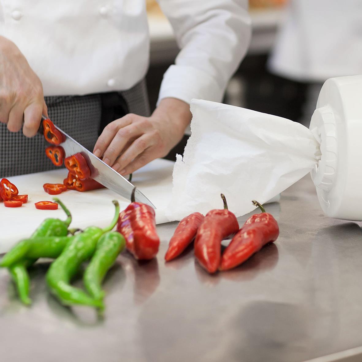 Person skär röd och grön paprika på ett köksbord med vit pappersrulle i bakgrunden