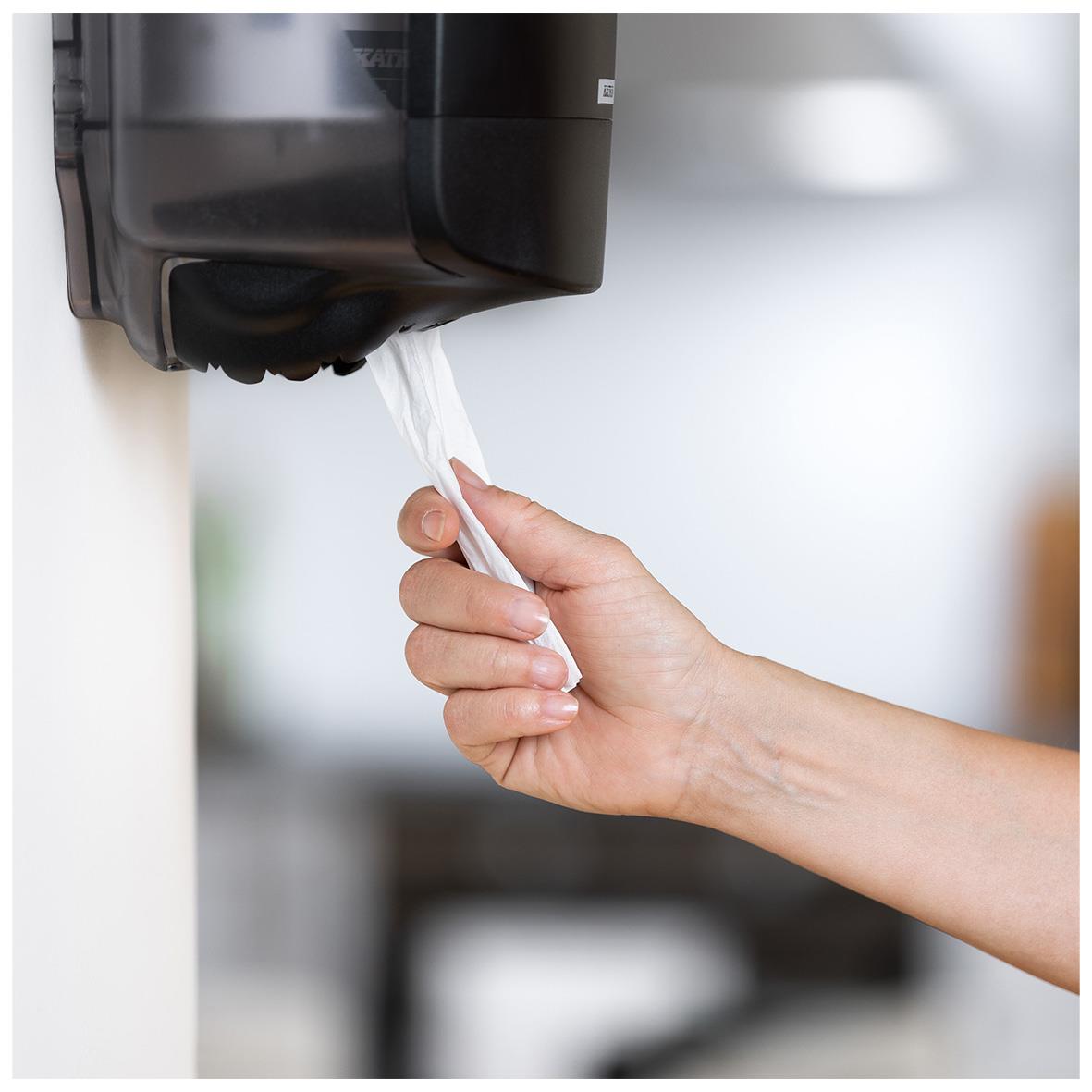 Hand som drar ut Katrin S Plus 2-lag vit torkrulle ur dispenser