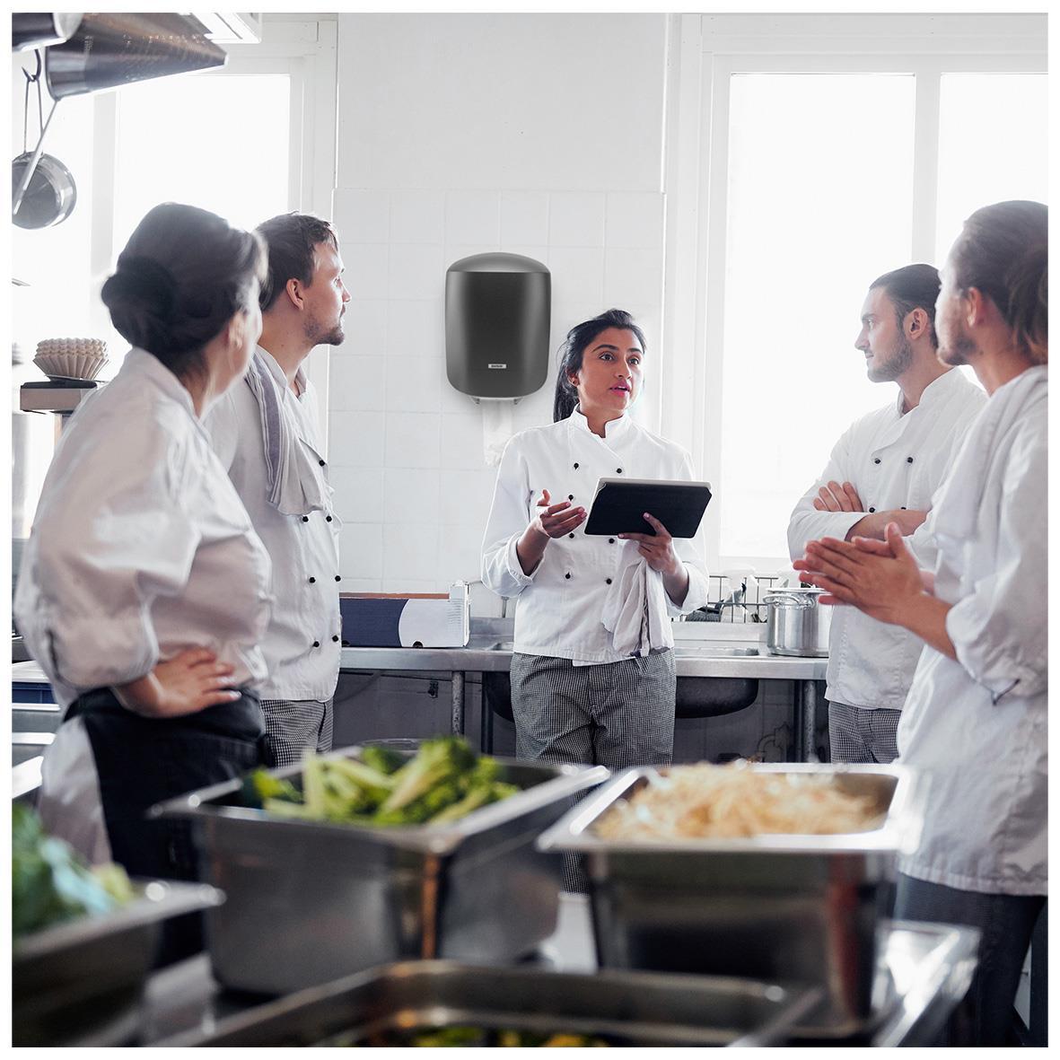 Köks- eller restaurangpersonal i diskussion, klädda i vita arbetskläder i ett kök med storkökstextilier