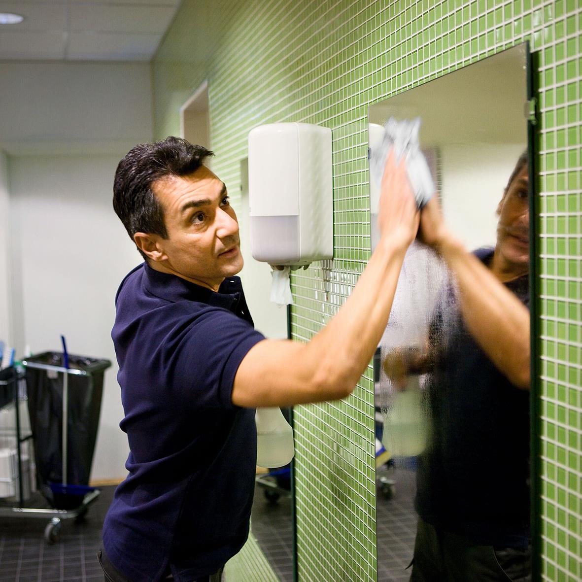 Man torkar spegel i badrum med vit vägg och handduksrulle