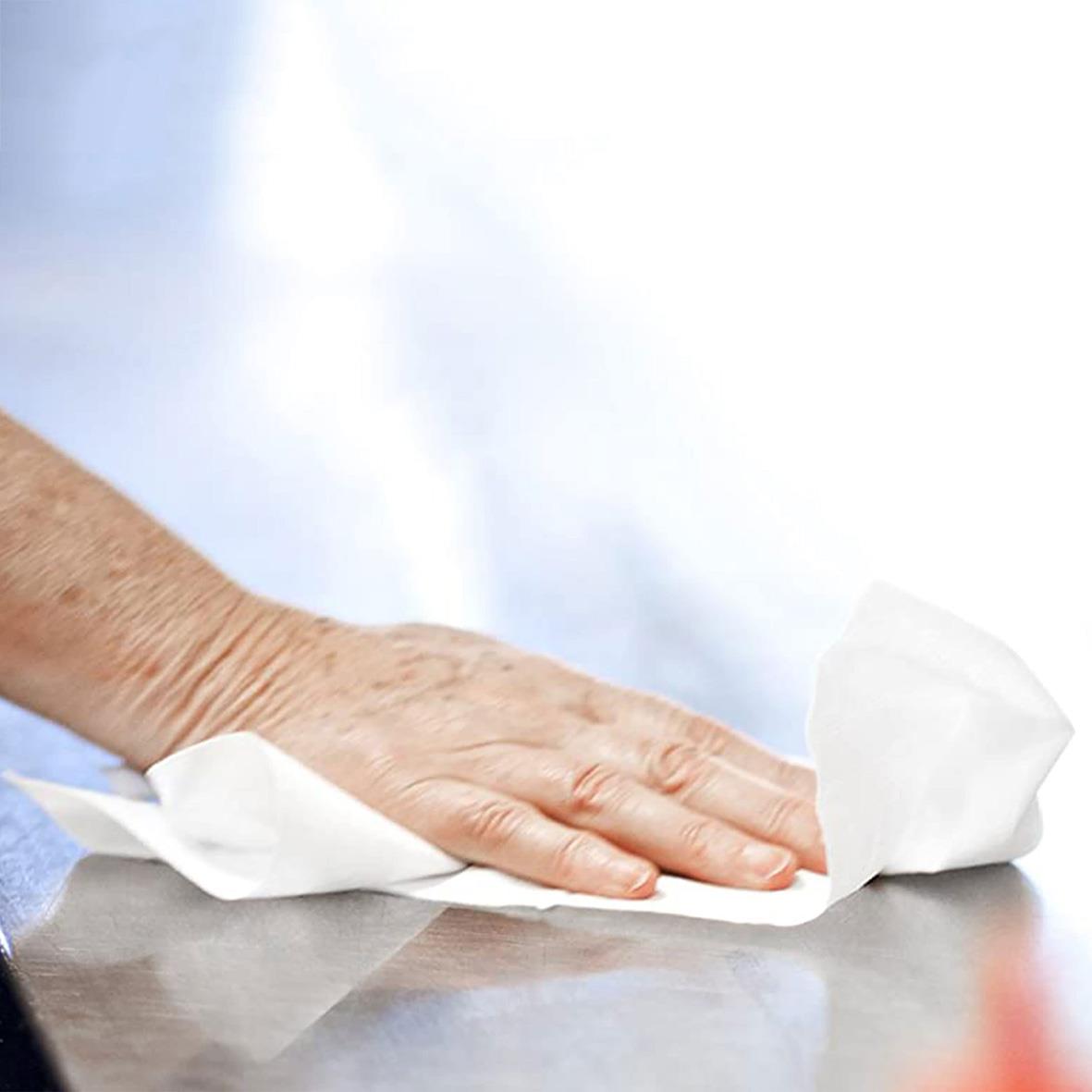 Person torkar en yta med vit pappersrulle på ett bord