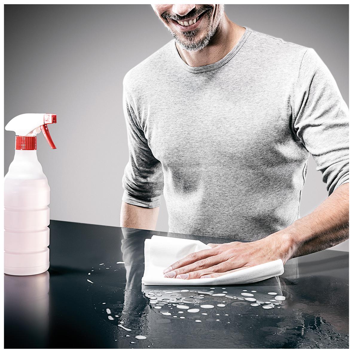 Man torkar av en svart yta med en vit Torkduk Katrin FlexMaster 1-lag, 42x35,5cm, med sprayflaska bredvid