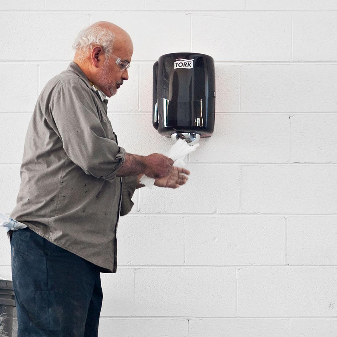 Man använder dispenser för Torkrulle Tork M2 centrummatad i rött och svart monterad på vägg