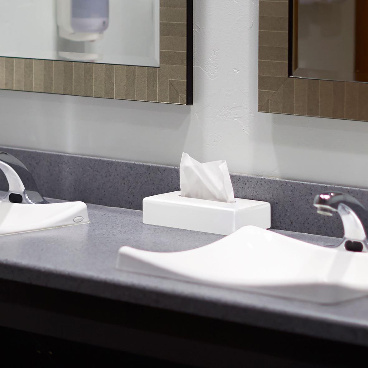 Vitt ansiktsservett dispenser på badrumsskrivbord med speglar i bakgrunden
